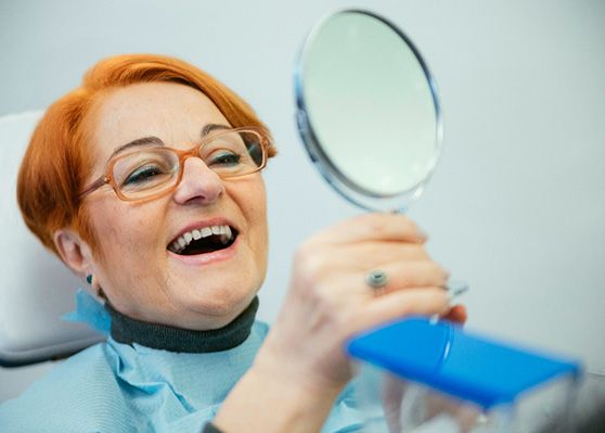 Older woman looking at her smile in the mirror at dentist’s office