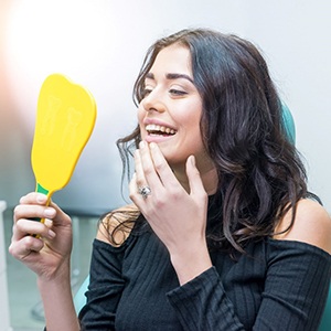 Woman smiling at reflection in handheld mirror