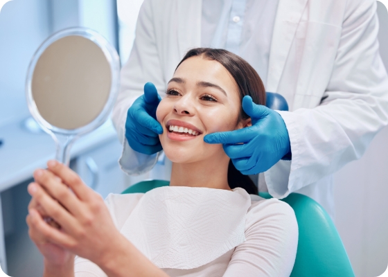 Young woman in dental chair looking at her smile in mirror