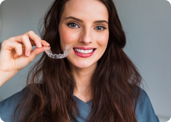Smiling brunette woman holding a clear aligner