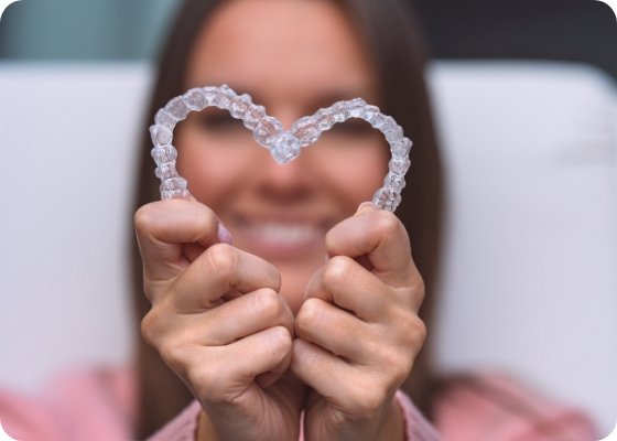 Woman holding two clear aligners in the shape of a heart