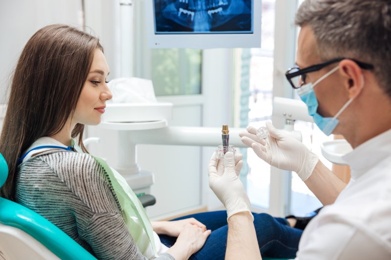 A male dentist showing a dental implant to his female patient